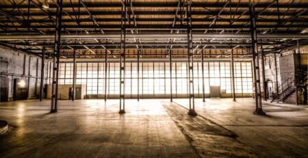 Es ist eine leere Lagerhalle zu sehen in der das Sonnenlicht leicht durch die verschmutzten Fenster scheint