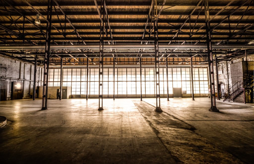 Es ist eine leere Lagerhalle zu sehen in der das Sonnenlicht leicht durch die verschmutzten Fenster scheint