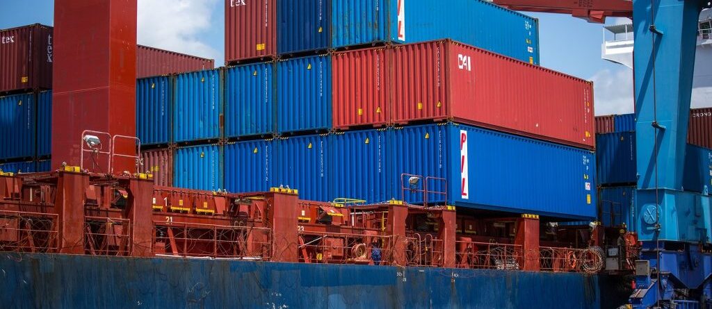 Es sind Container auf einem Containerschiff zu sehen das in einem Containerhafen anliegt.