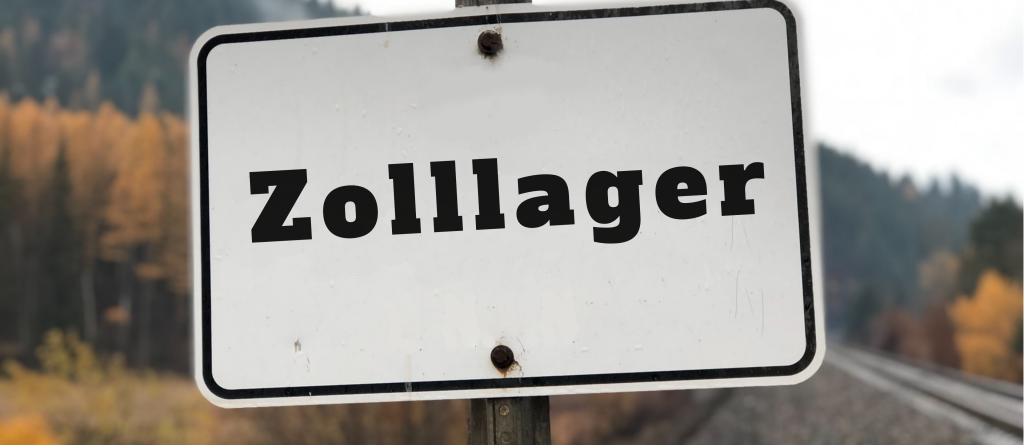 Im Vordergrund ist ein Schild zu sehen auf dem Zolllager steht, der Hintergrund ist unscharf, man Sieht Bäume und eine Bahnschiene