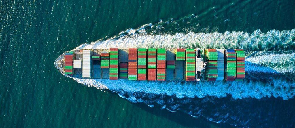 Ein Container aus der Vogelperspektive das in türkis-blauen Meereswasser fährt