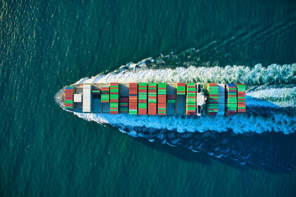 Ein Container aus der Vogelperspektive das in türkis-blauen Meereswasser fährt